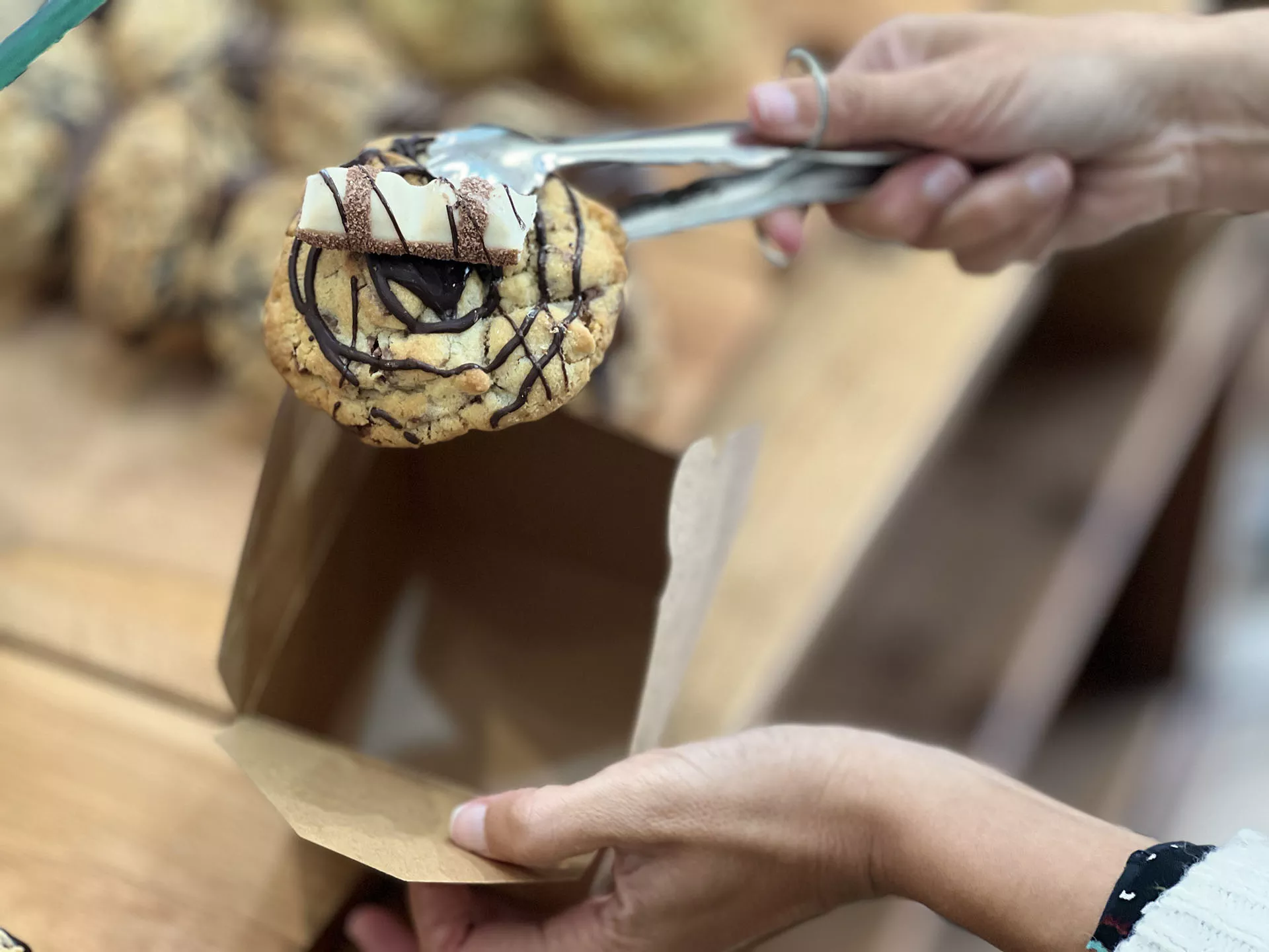 Manos sosteniendo con una pinza una cookie y la otra mano una caja, cookies de fondo