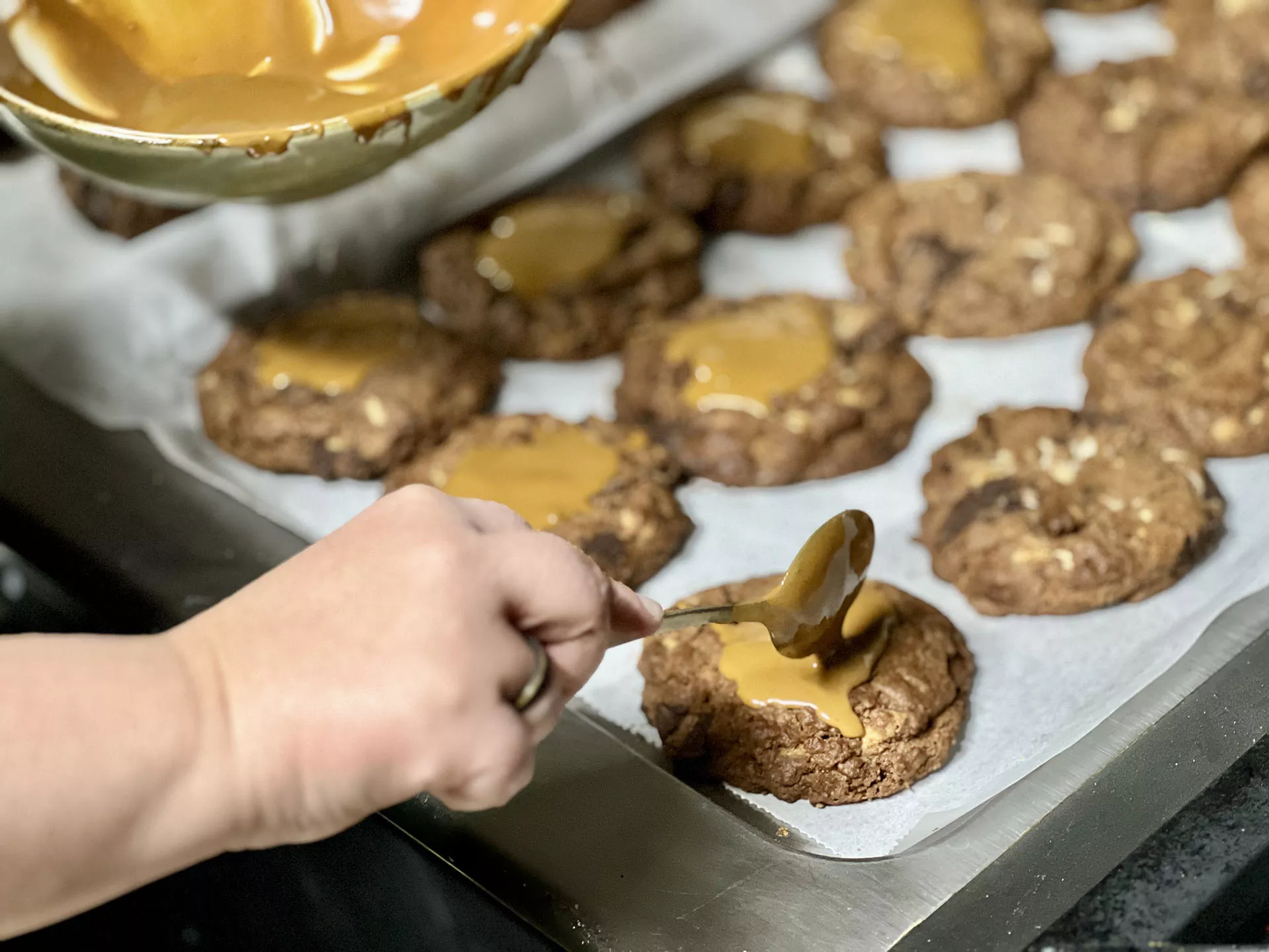 Mano decorando cookie con una cuchara, varias cookies ya terminadas en bandeja